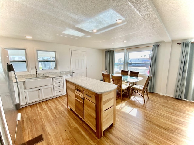 kitchen with white cabinetry, sink, a textured ceiling, and light hardwood / wood-style flooring