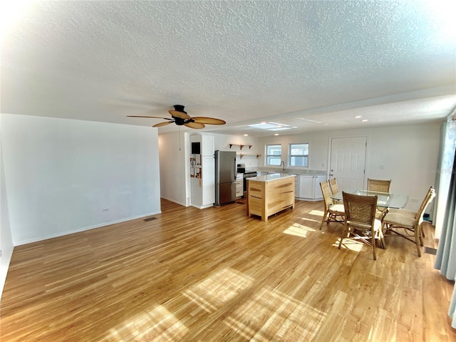 kitchen featuring light hardwood / wood-style flooring, ceiling fan, a textured ceiling, light brown cabinetry, and appliances with stainless steel finishes