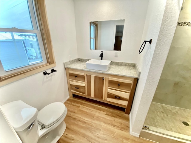 bathroom with a tile shower, hardwood / wood-style floors, vanity, and toilet