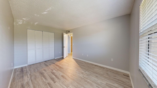 unfurnished bedroom with light wood-type flooring, a textured ceiling, and a closet