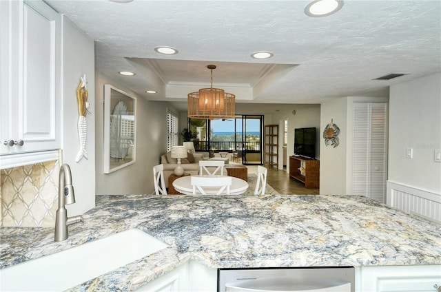 kitchen with light stone counters, a raised ceiling, sink, decorative light fixtures, and white cabinets