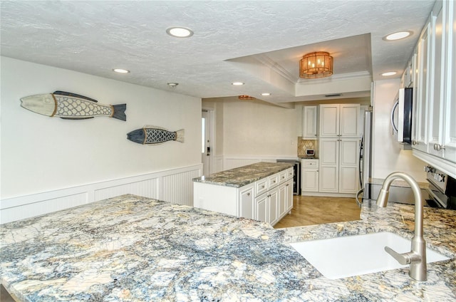 kitchen with white cabinets, sink, ornamental molding, a kitchen island, and stainless steel appliances