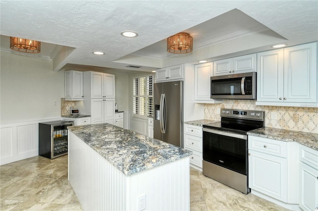 kitchen with white cabinets, wine cooler, a kitchen island, light stone counters, and stainless steel appliances