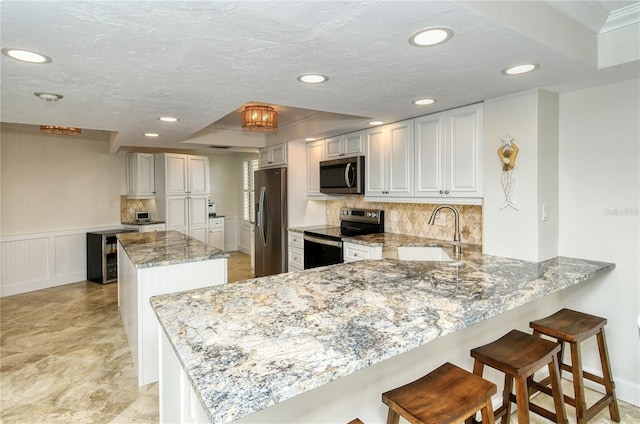 kitchen with sink, tasteful backsplash, kitchen peninsula, white cabinets, and appliances with stainless steel finishes