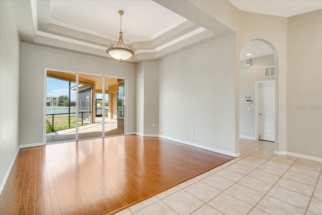 empty room featuring light wood-type flooring, a raised ceiling, and crown molding