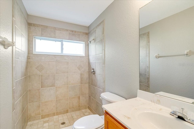 bathroom with tiled shower, vanity, and toilet