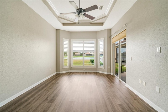 unfurnished room with a tray ceiling, dark hardwood / wood-style floors, ornamental molding, and ceiling fan