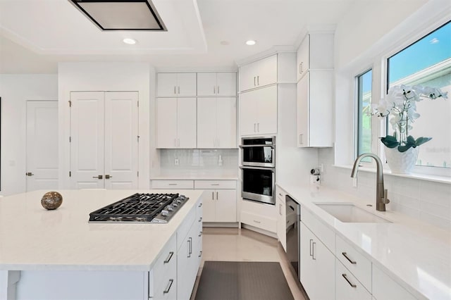 kitchen featuring backsplash, stainless steel appliances, sink, a center island, and white cabinetry