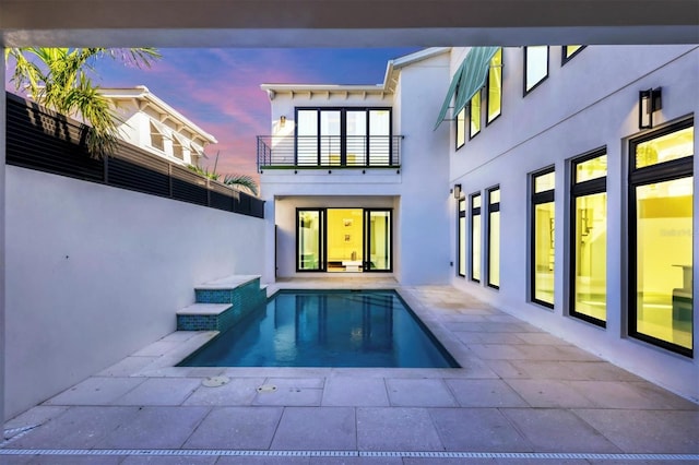 back house at dusk featuring a swimming pool with hot tub and a balcony