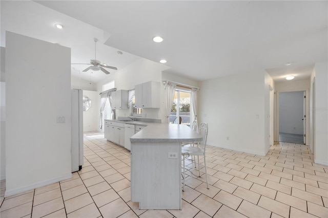 kitchen featuring light tile patterned floors, sink, ceiling fan, white cabinetry, and a kitchen breakfast bar