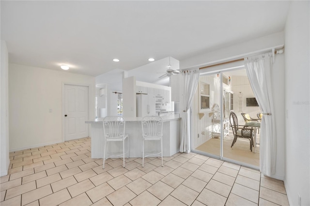 kitchen with white cabinetry, ceiling fan, a kitchen breakfast bar, kitchen peninsula, and white appliances