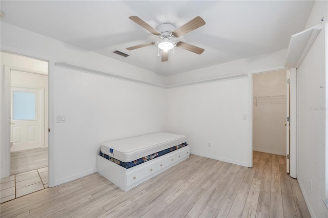 bedroom featuring a walk in closet, ceiling fan, and light hardwood / wood-style flooring