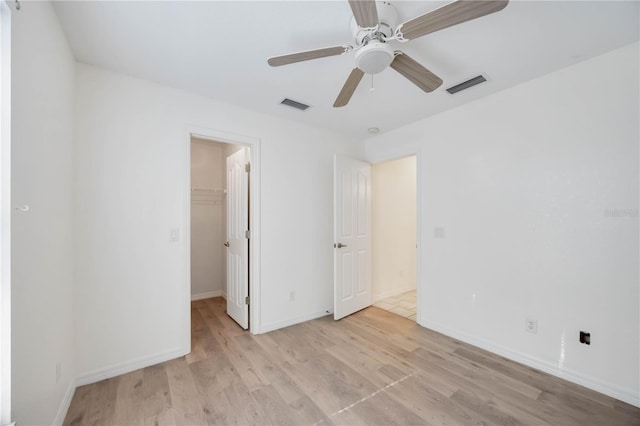 unfurnished bedroom featuring a walk in closet, light hardwood / wood-style floors, a closet, and ceiling fan