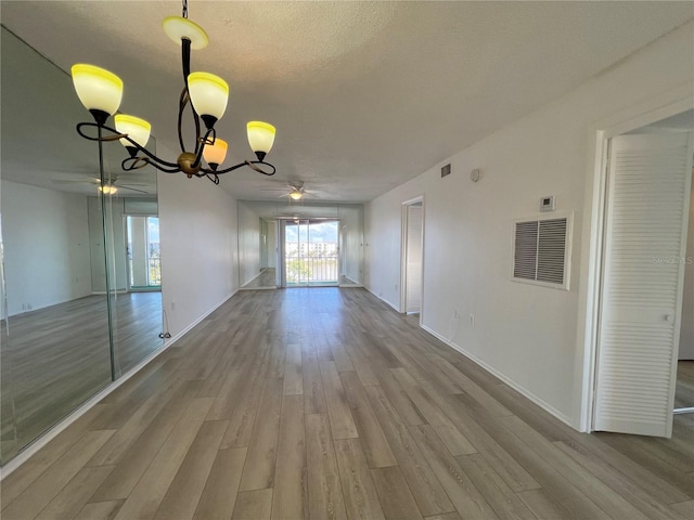 unfurnished dining area featuring ceiling fan with notable chandelier, light hardwood / wood-style flooring, and a textured ceiling