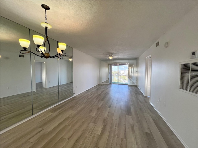 empty room with wood-type flooring, ceiling fan with notable chandelier, and a textured ceiling