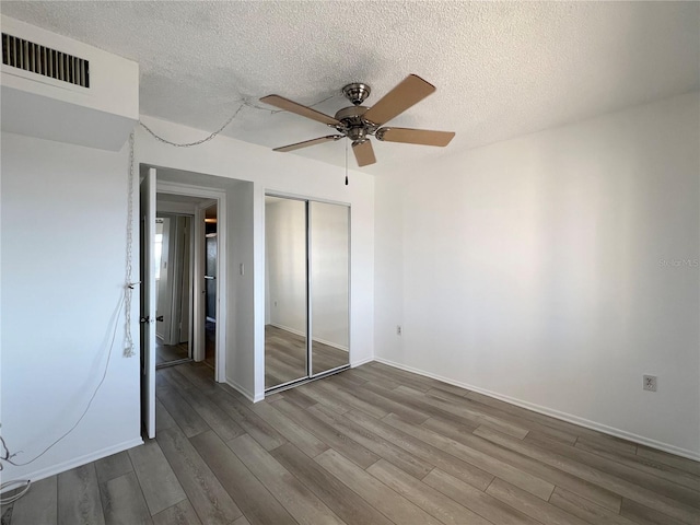 unfurnished bedroom with ceiling fan, hardwood / wood-style floors, a closet, and a textured ceiling