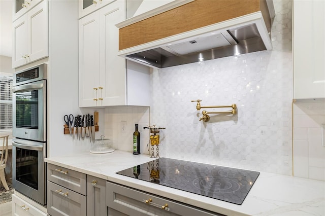 kitchen with black electric stovetop, white cabinets, stainless steel double oven, and custom range hood