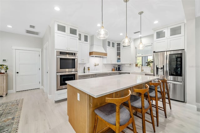 kitchen featuring appliances with stainless steel finishes, custom range hood, a kitchen island, sink, and white cabinetry