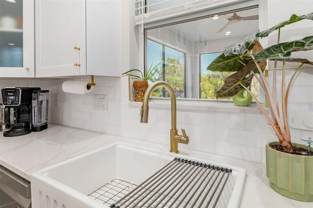 kitchen featuring light stone countertops, backsplash, white cabinetry, and sink