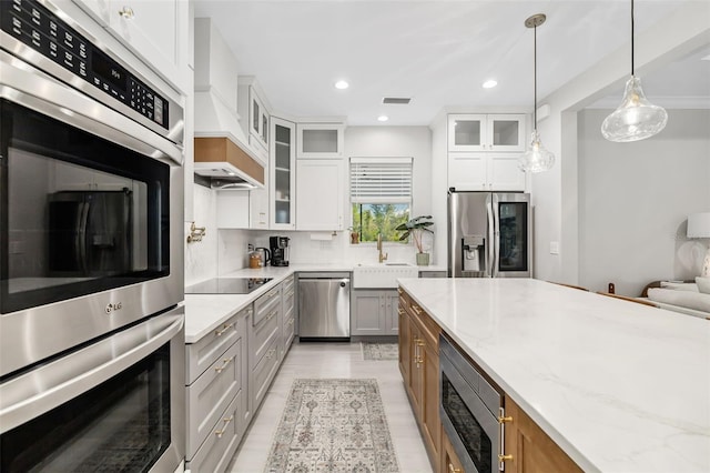 kitchen featuring white cabinets, sink, appliances with stainless steel finishes, decorative light fixtures, and light stone counters