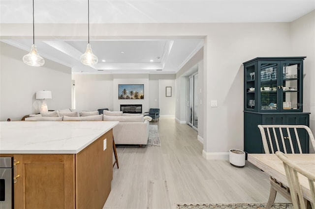 kitchen featuring light wood-type flooring, a tray ceiling, light stone counters, and hanging light fixtures