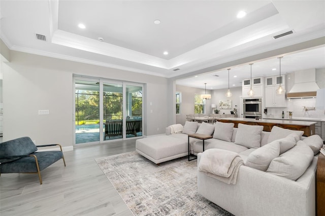 living room featuring light wood-type flooring, a raised ceiling, and ornamental molding