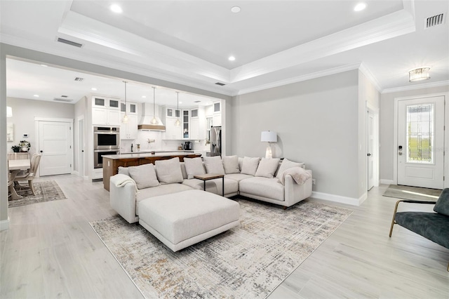 living room featuring a raised ceiling, crown molding, and light wood-type flooring