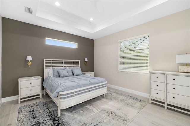 bedroom with ceiling fan, light hardwood / wood-style floors, and a tray ceiling