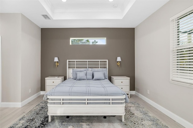 bedroom with a tray ceiling, ornamental molding, and light wood-type flooring