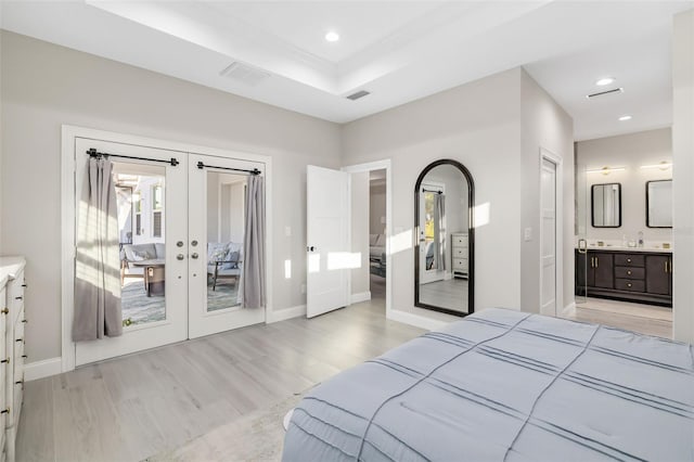 bedroom with ensuite bathroom, light hardwood / wood-style flooring, a tray ceiling, and french doors