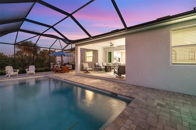 pool at dusk with an outdoor hangout area, glass enclosure, ceiling fan, and a patio area