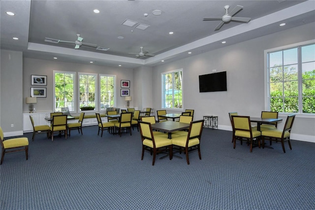 dining area with a tray ceiling, dark carpet, and ceiling fan