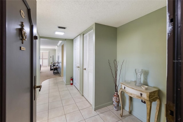 hallway with a textured ceiling and light tile patterned flooring