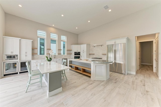 kitchen featuring white cabinetry, a center island, beverage cooler, and appliances with stainless steel finishes