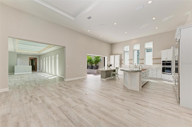 kitchen with a kitchen breakfast bar, a center island with sink, white cabinetry, and a tray ceiling