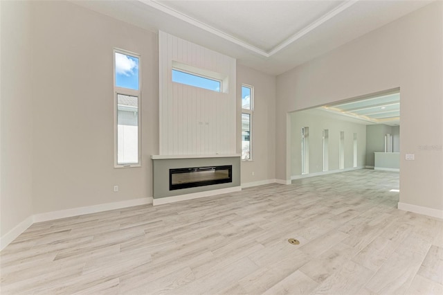 unfurnished living room with light hardwood / wood-style floors, crown molding, and a tray ceiling