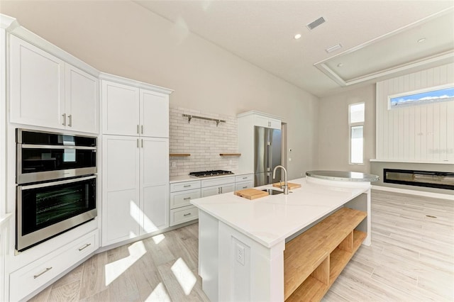 kitchen with a kitchen island with sink, white cabinets, sink, light wood-type flooring, and appliances with stainless steel finishes