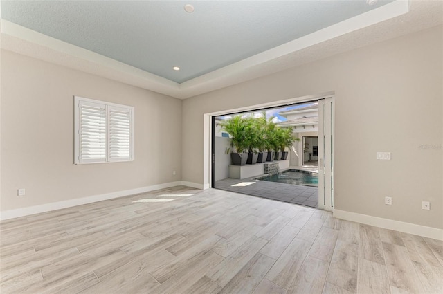 unfurnished room featuring a tray ceiling, a textured ceiling, and light wood-type flooring