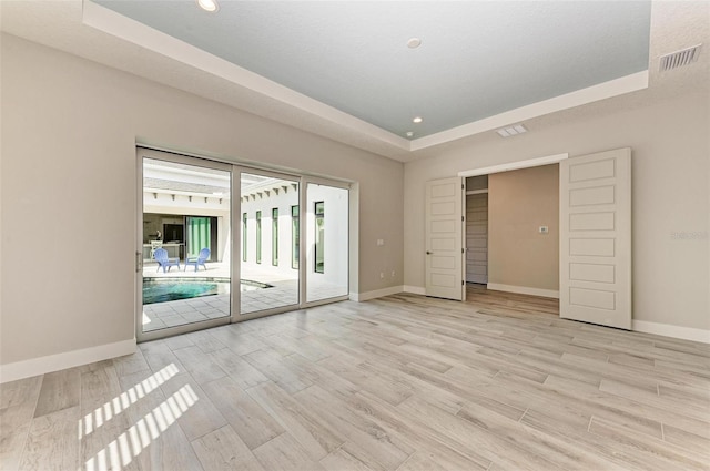 spare room featuring a tray ceiling and light hardwood / wood-style floors