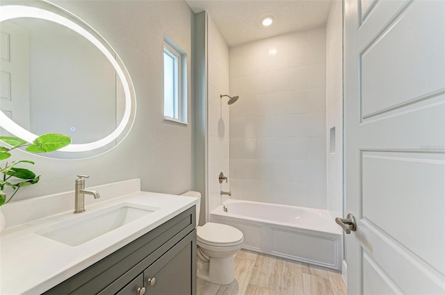 full bathroom featuring vanity, hardwood / wood-style flooring, tiled shower / bath combo, toilet, and a textured ceiling