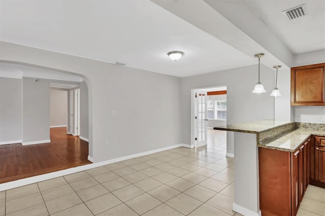 kitchen with kitchen peninsula, light stone counters, hanging light fixtures, and light hardwood / wood-style floors