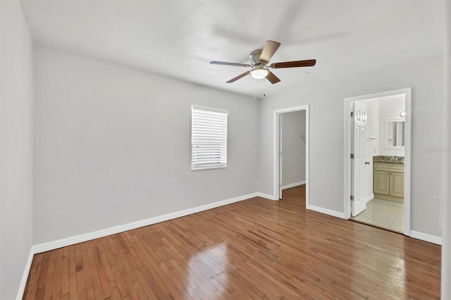 unfurnished bedroom with a walk in closet, light wood-type flooring, ensuite bathroom, ceiling fan, and a closet