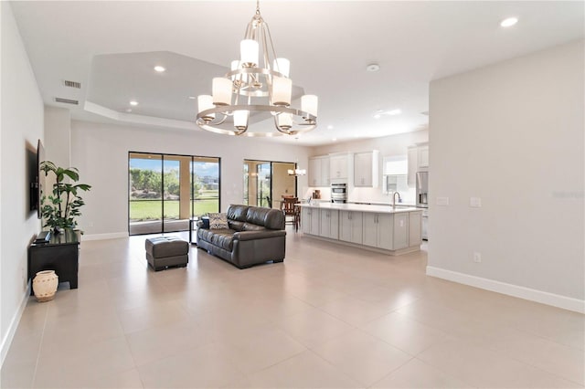 living room featuring light tile patterned flooring, an inviting chandelier, a raised ceiling, and sink