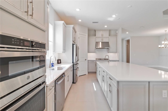 kitchen with appliances with stainless steel finishes, a kitchen island with sink, sink, decorative light fixtures, and an inviting chandelier