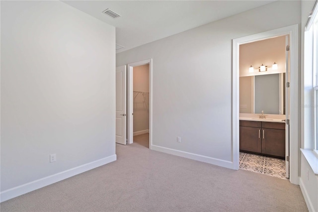 unfurnished bedroom featuring ensuite bath, light colored carpet, sink, a spacious closet, and a closet