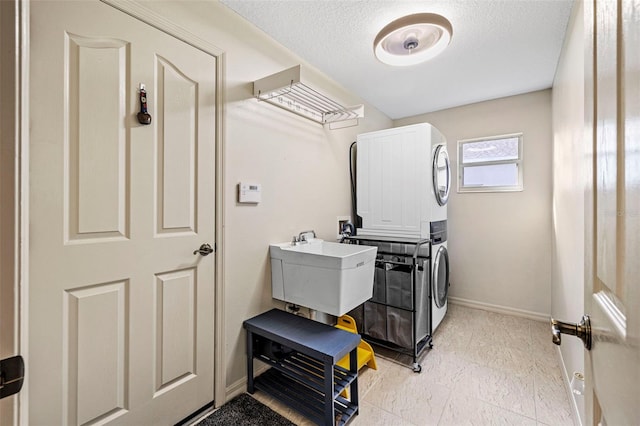 washroom featuring a textured ceiling, stacked washing maching and dryer, and sink