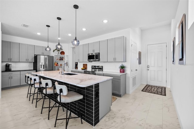 kitchen featuring gray cabinetry, backsplash, a kitchen island with sink, sink, and stainless steel appliances