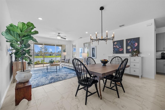 dining room with ceiling fan with notable chandelier and a water view