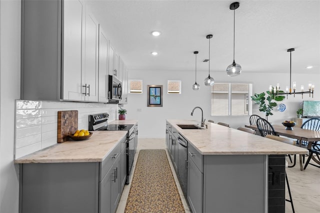 kitchen with appliances with stainless steel finishes, sink, pendant lighting, gray cabinets, and an island with sink