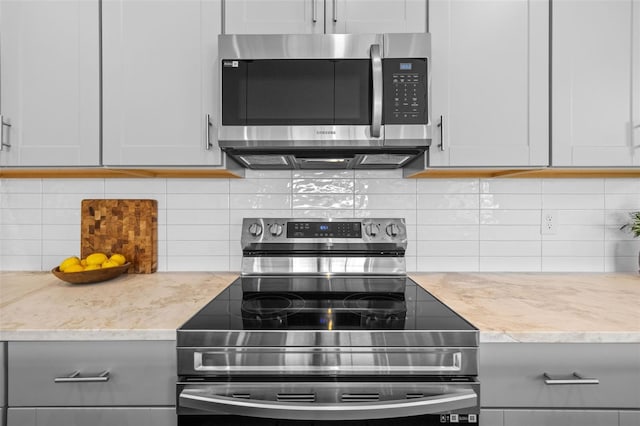 kitchen with appliances with stainless steel finishes, tasteful backsplash, light stone counters, and white cabinetry